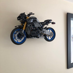 Peut inclure: Un mod&egrave;le de moto LEGO noir et gris avec des roues bleues. La moto est mont&eacute;e sur un mur.