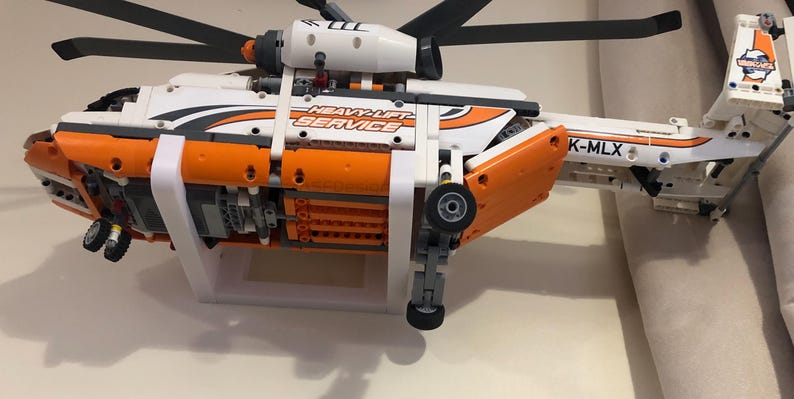 May include: A white and orange Lego helicopter model with the text "Heavy-Lift Service" and "K-MLX" on the side. The helicopter is mounted on a white stand.