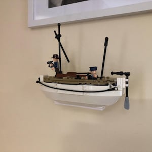 May include: A white Lego boat with two Lego figures on board. The boat has a black mast and a black oar. The figures are wearing brown and blue clothing.