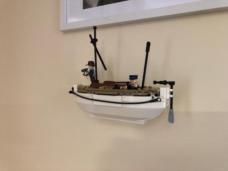 May include: A white Lego boat with two Lego figures on board. The boat has a black mast and a black oar. The figures are wearing brown and blue clothing.
