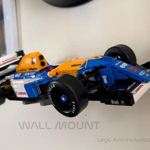 May include: A blue, yellow, and white toy race car with black tires. The car has sponsor logos and the text "Canon" and "Williams". The words "WALL MOUNT" are below the car.