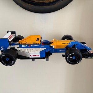 May include: A blue and yellow race car model with black wheels. The model has the number 5 on the side and the words "Goodyear", "Williams", "Canon", and "Renault" printed on it. The car is a toy.