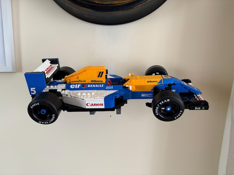 May include: A blue and yellow race car model with black wheels. The model has the number 5 on the side and the words "Goodyear", "Williams", "Canon", and "Renault" printed on it. The car is a toy.