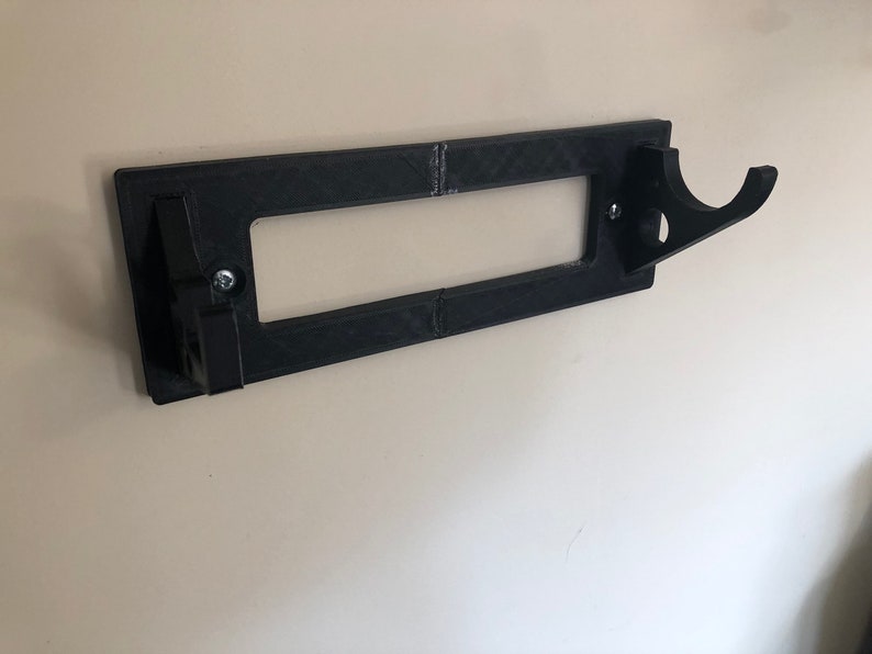 May include: A black plastic wall mount with a hook for hanging items. The mount has a rectangular opening in the center.