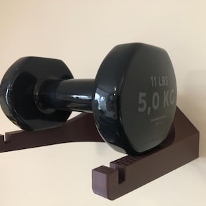 May include: A black dumbbell with a brown wall mount. The dumbbell weighs 11 lbs or 5.0 kg.