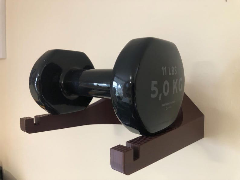 May include: A black dumbbell with a brown wall mount. The dumbbell weighs 11 lbs or 5.0 kg.