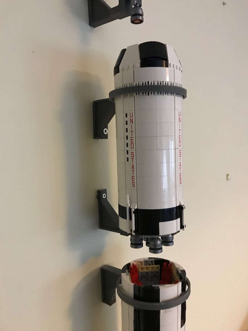 May include: A white and black Lego model of a rocket ship with the words "UNITED STATES" printed on the side. The rocket is mounted on a gray wall mount.