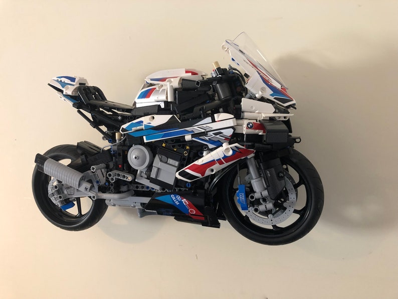 May include: A white, blue, and red LEGO&reg; Technic&trade; BMW M 1000 RR motorcycle model with a black engine and a clear windshield.