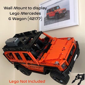 May include: A wall mount for displaying a Lego Mercedes G Wagon (42177). The mount is made of black plastic and has a metal bracket. The Lego model is orange and black and is not included.