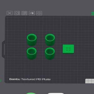 Op de afbeelding: Een 3D-weergave van vier groene cilindrische objecten en een klein groen vierkant met cirkelvormige inkepingen. De objecten zijn gerangschikt op een donkergrijs raster, met de tekst "Bambu Textured PEI Plate" onderaan.