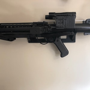 May include: A black plastic toy blaster with a scope and a handle. The blaster is mounted on a wall.