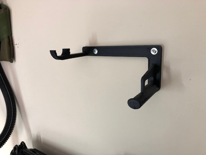 May include: A black, wall-mounted bracket with two curved supports and a cylindrical end. The bracket is secured to the wall with two screws. The design is simple and functional, likely for holding an item.