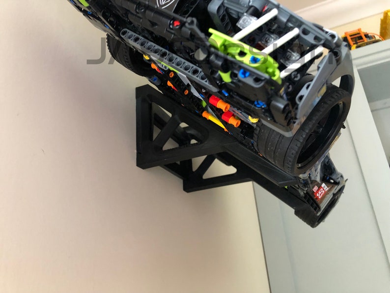 Pu&ograve; includere: Un modello di auto Lego nero montato su un supporto da parete nero. L'auto &egrave; capovolta e ha uno schema di colori verde e nero. Il supporto da parete ha una forma triangolare.