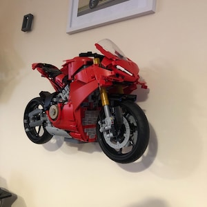 May include: A red Lego motorcycle model mounted on a wall. The motorcycle has a black windshield and black wheels.