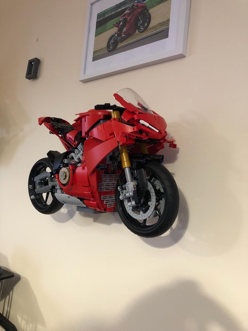 May include: A red Lego motorcycle model mounted on a wall. The motorcycle has a black windshield and black wheels.
