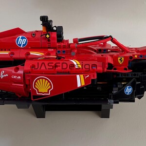May include: A red and black Lego Ferrari Formula 1 race car with the logos "V-Power", "Ray-Ban", "Shell", and "HP" on the side. The car is on a white background.