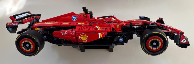 May include: A red and black Lego Ferrari Formula 1 race car with the logos "V-Power", "Ray-Ban", "Shell", and "HP" on the side. The car is on a white background.