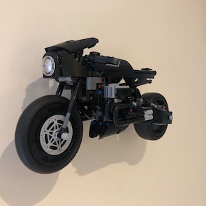 May include: A black Lego motorcycle model with a detailed engine and wheels. The motorcycle is mounted on a wall.