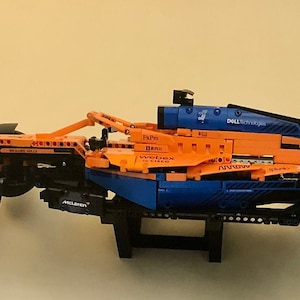 May include: A blue and orange Lego McLaren Formula 1 race car model with the text "DELL Technologies" on the side. The car is on a black stand.