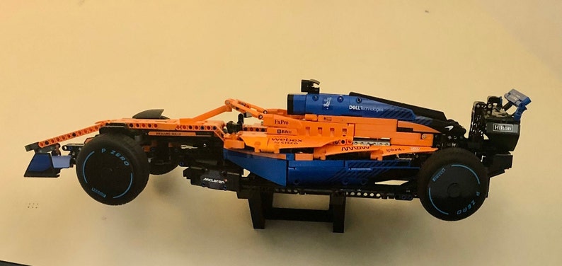 May include: A blue and orange Lego McLaren Formula 1 race car model with the text "DELL Technologies" on the side. The car is on a black stand.