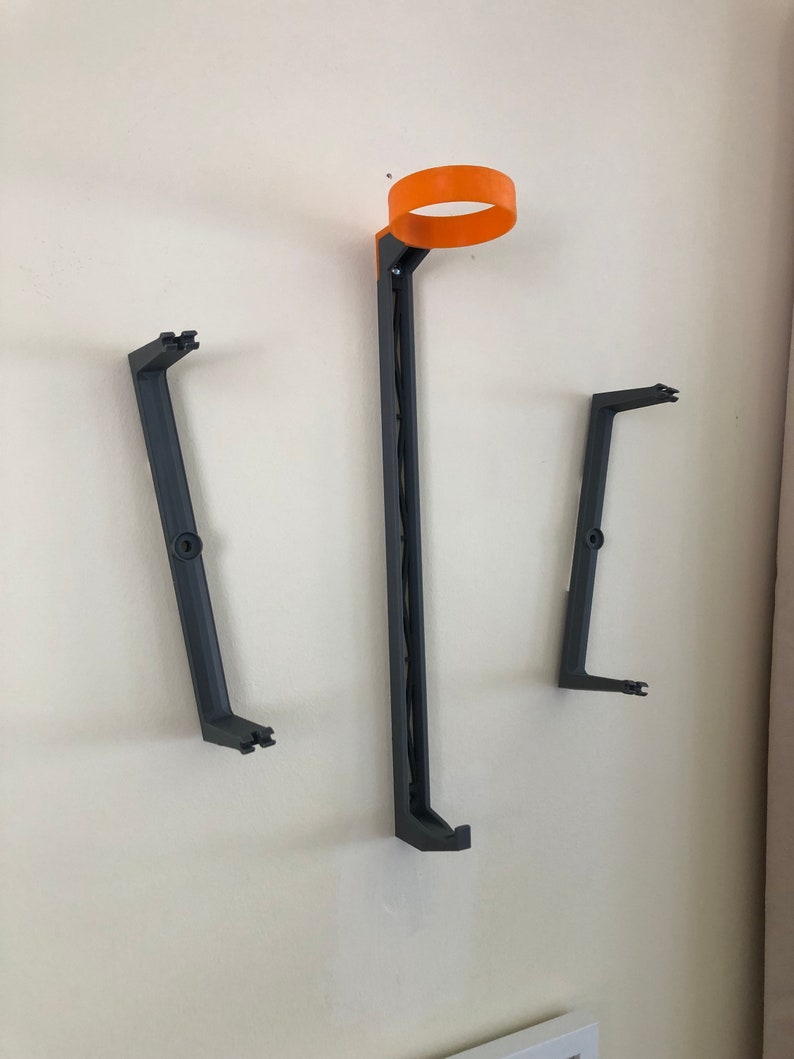 May include: Three wall-mounted black plastic holders for a 3D printer filament spool. The top holder has an orange ring.