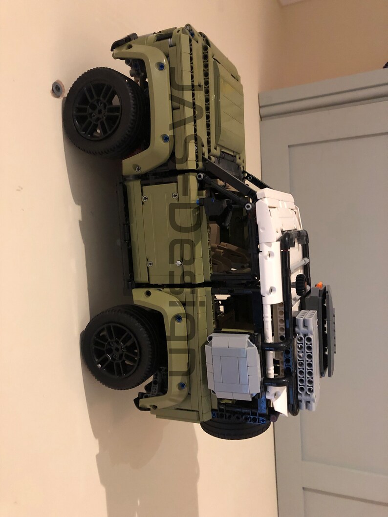 May include: A green Lego Land Rover Defender model with black wheels and a white roof. The model is mounted on a wall.
