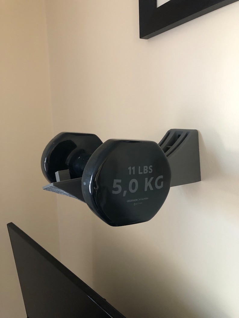 May include: Black dumbbell weight rack mounted on a wall with a 11 lbs / 5.0 kg dumbbell in place.