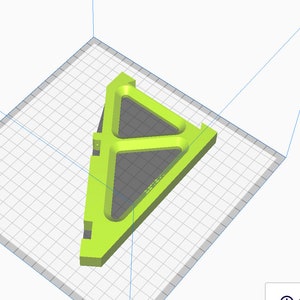 May include: A bright green, triangular 3D-printed object with a hollow interior and rounded edges. The object sits on a gray grid, suggesting a design or modeling environment. The design features a central triangular opening.