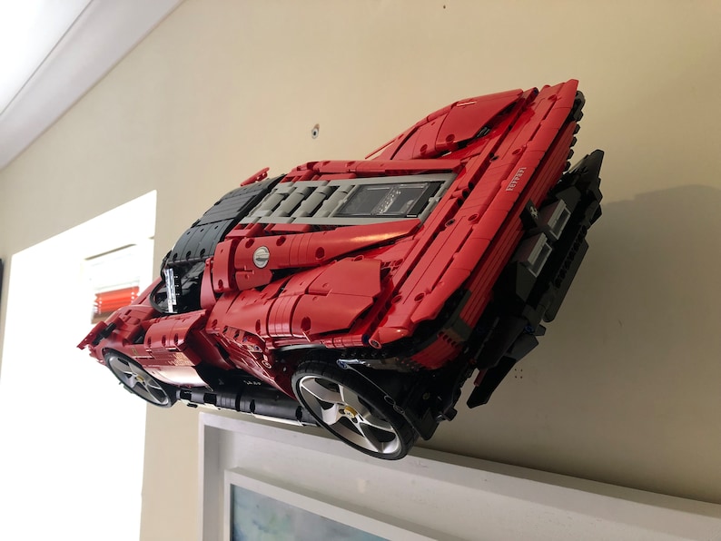 May include: A red Lego Ferrari LaFerrari model car with black and grey details. The car is mounted on a wall and is facing the camera.