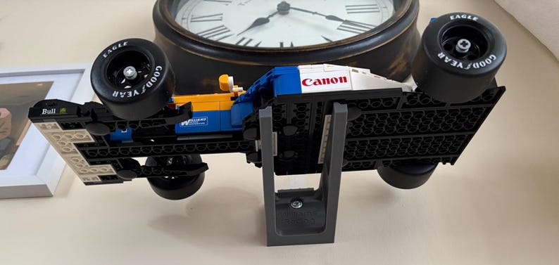 May include: A Lego race car model in blue, yellow, and white, with "Canon" printed on the top. The car has black tires with "Goodyear" and "Eagle" branding. The model is displayed on a gray stand.