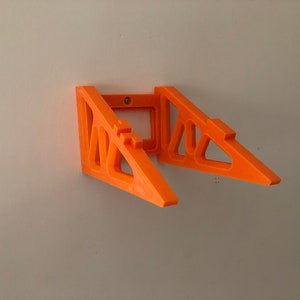 Puede incluir: Soportes de estante naranja montados en la pared. Los soportes son de pl&aacute;stico y tienen un dise&ntilde;o geom&eacute;trico. Los soportes est&aacute;n montados en una pared blanca. Los soportes est&aacute;n dise&ntilde;ados para sostener un estante.