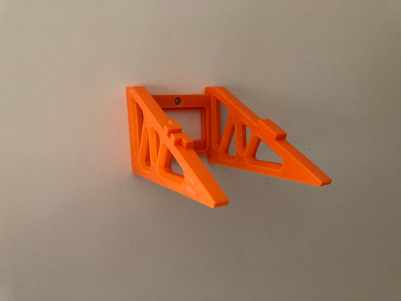 Puede incluir: Soportes de estante naranja montados en la pared. Los soportes son de pl&aacute;stico y tienen un dise&ntilde;o geom&eacute;trico. Los soportes est&aacute;n montados en una pared blanca. Los soportes est&aacute;n dise&ntilde;ados para sostener un estante.