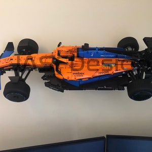 May include: A Lego model of a McLaren Formula 1 race car with sponsors including Dell Technologies, Webex by Cisco, and Hilton. The car is orange and blue with black wheels.