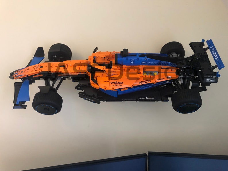 May include: A Lego model of a McLaren Formula 1 race car with sponsors including Dell Technologies, Webex by Cisco, and Hilton. The car is orange and blue with black wheels.