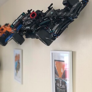 May include: Two black Formula 1 race cars mounted on a wall. The cars are black with green and silver accents. The cars are labeled "PETRONAS" and "MERCEDES".