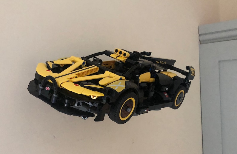 May include: A yellow and black Lego Technic model car with a W10.4 sticker on the side. The car has a black chassis and yellow bodywork with black stripes. The car has a black spoiler and a black rear diffuser.