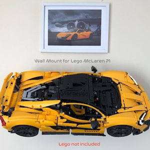 May include: A yellow Lego McLaren P1 model mounted on a wall. The model is a detailed replica of the sports car. Above the model is a framed picture of the real car. The text "Wall Mount for Lego McLaren P1" is above the model. The text "Lego not included" is below the model.