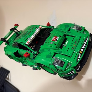 May include: A bright green Lego Porsche race car model with black accents and the word "PORSCHE" on the spoiler. The car features a shark-like design on the front and the number "77".