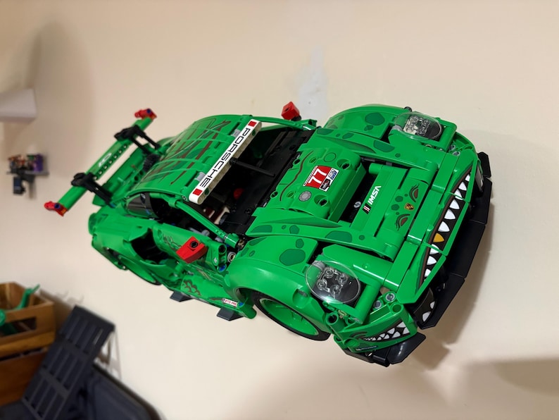 May include: A bright green Lego Porsche race car model with black accents and the word "PORSCHE" on the spoiler. The car features a shark-like design on the front and the number "77".