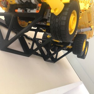 K&ouml;nnte beinhalten: Ein schwarzer 3D-gedruckter Wandhalter, der f&uuml;r das Halten eines Spielzeuglastwagens konzipiert ist. Der Halter besteht aus mehreren dreieckigen Teilen, die ineinandergreifen, um eine stabile Struktur zu bilden. Der Halter ist an einer wei&szlig;en Wand befestigt und ein gelber Spielzeuglastwagen ruht auf dem Halter.