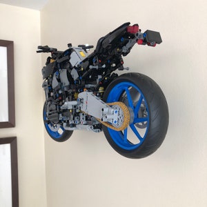 Peut inclure: Un mod&egrave;le LEGO d&eacute;taill&eacute; d'une moto avec un cadre noir, des roues bleues et une cha&icirc;ne dor&eacute;e. La moto est mont&eacute;e sur un mur.