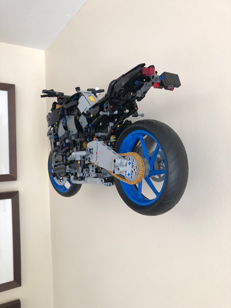 Peut inclure: Un mod&egrave;le LEGO d&eacute;taill&eacute; d'une moto avec un cadre noir, des roues bleues et une cha&icirc;ne dor&eacute;e. La moto est mont&eacute;e sur un mur.