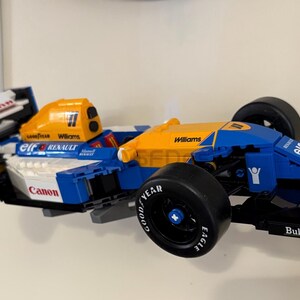 May include: A blue, white, and yellow Lego model of a Formula 1 race car. The car features sponsor logos, black tires, and the number 5. The model is a detailed replica of a Williams Renault race car.