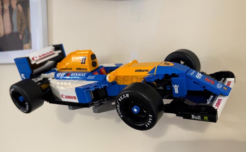 May include: A blue, white, and yellow Lego model of a Formula 1 race car. The car features sponsor logos, black tires, and the number 5. The model is a detailed replica of a Williams Renault race car.