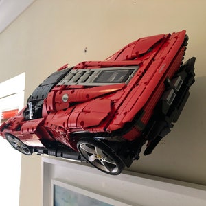 May include: A red Lego Ferrari LaFerrari model car with black and gray details. The car is mounted on a wall and is facing the camera.
