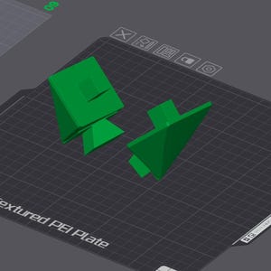 K&ouml;nnte beinhalten: Zwei gr&uuml;n bedruckte 3D-Objekte auf einer strukturierten schwarzen Oberfl&auml;che. Die Objekte sind geometrische Formen mit scharfen Kanten.