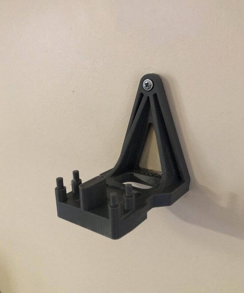May include: A black 3D printed wall mount with a triangular design and a rectangular base. The mount has several small holes on the base and a single screw hole at the top.