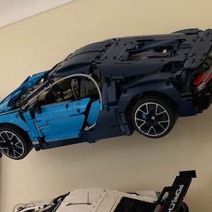 May include: A blue and black Lego Bugatti Chiron model car is mounted on a wall. The car is suspended in mid-air, with the wheels facing forward. The car has a detailed interior and exterior, including a working engine and a detailed dashboard.