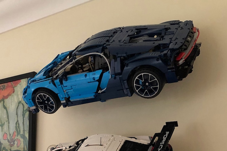 May include: A blue and black Lego Bugatti Chiron model car is mounted on a wall. The car is suspended in mid-air, with the wheels facing forward. The car has a detailed interior and exterior, including a working engine and a detailed dashboard.