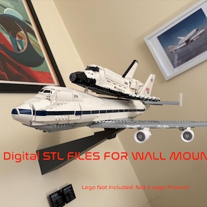 Op de afbeelding: Een wit en blauw model van een spaceshuttle gemonteerd op een wit en blauw vliegtuig. Het model wordt op een wandmontage getoond. De tekst "Digital STL FILES FOR WALL MOUNT" is rood zichtbaar. De tekst "Lego Not Included. Not a Lego Product" is ook zichtbaar.